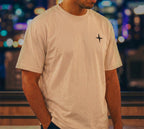 Model wearing beige colored oversized T-shirt with black north star logo on chest, casual oversized style, minneapolis skyline at night background