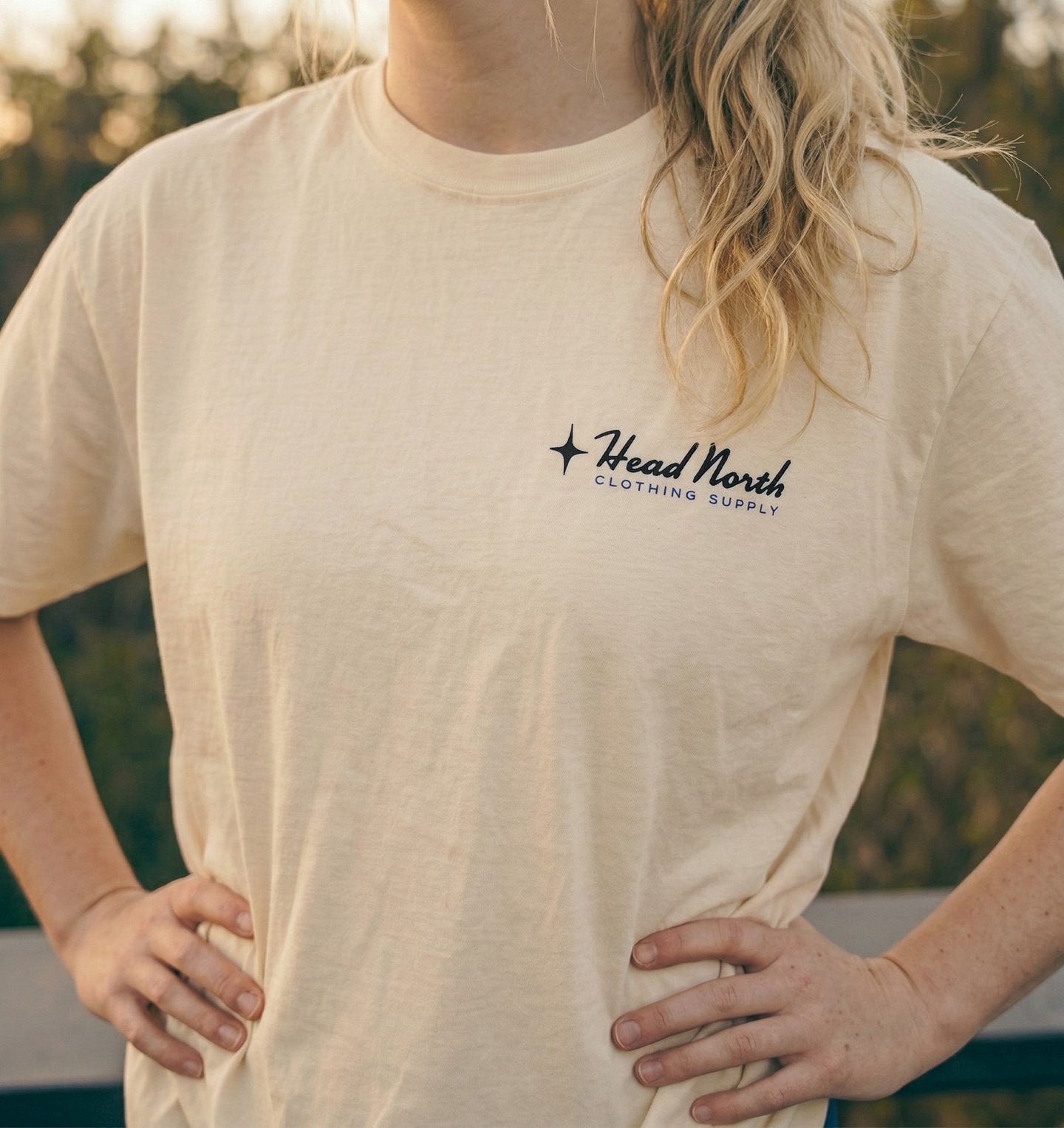 Model showing front of beige T-shirt with black and blue Head North Clothing Supply logo