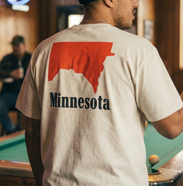 Model in a rural bar, wearing beige colored Minnesota shirt with a flipped, red Minnesota shape with Minnesota text underneath, inspired by Marlboro logo