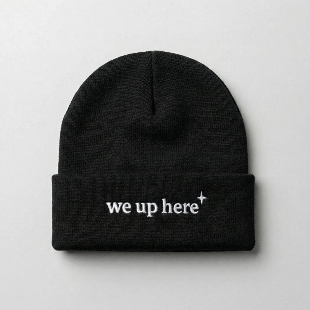 Black cuffed beanie with "we up here" embroidered in white text, and a small white north star accent